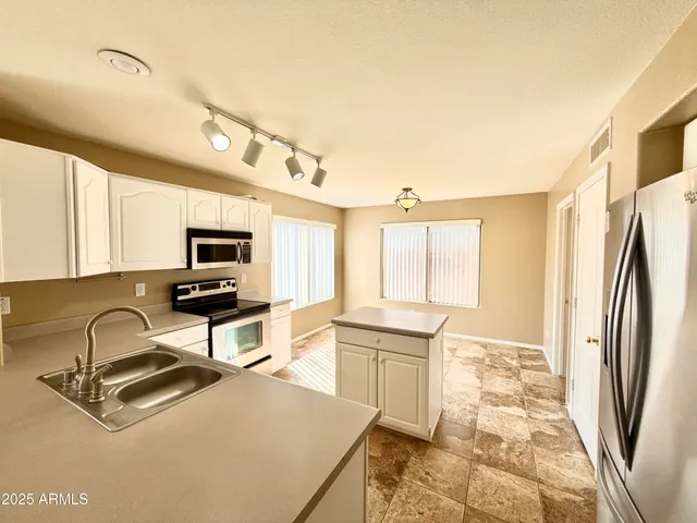 a room with stainless steel appliances a sink a stove a refrigerator cabinets and a window