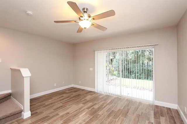 a view of an empty room with wooden floor and a ceiling fan
