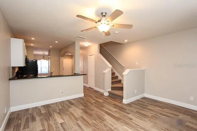 a view of an empty room with wooden floor and a ceiling fan