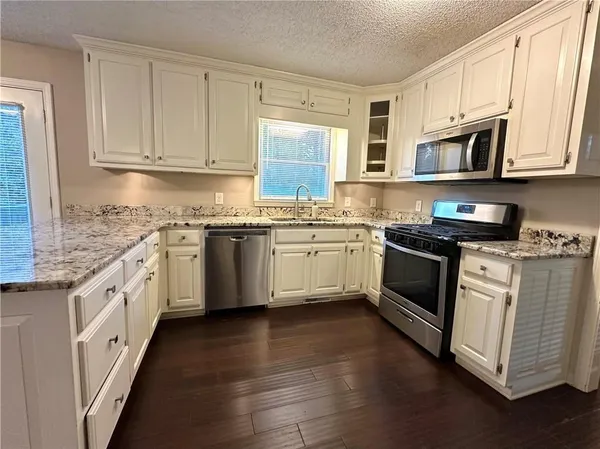 a kitchen with stainless steel appliances granite countertop a stove top oven a sink dishwasher and white cabinets with wooden floor