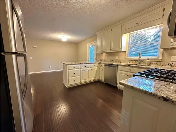 a kitchen with stainless steel appliances granite countertop a refrigerator a sink dishwasher a stove and white countertops with wooden floor