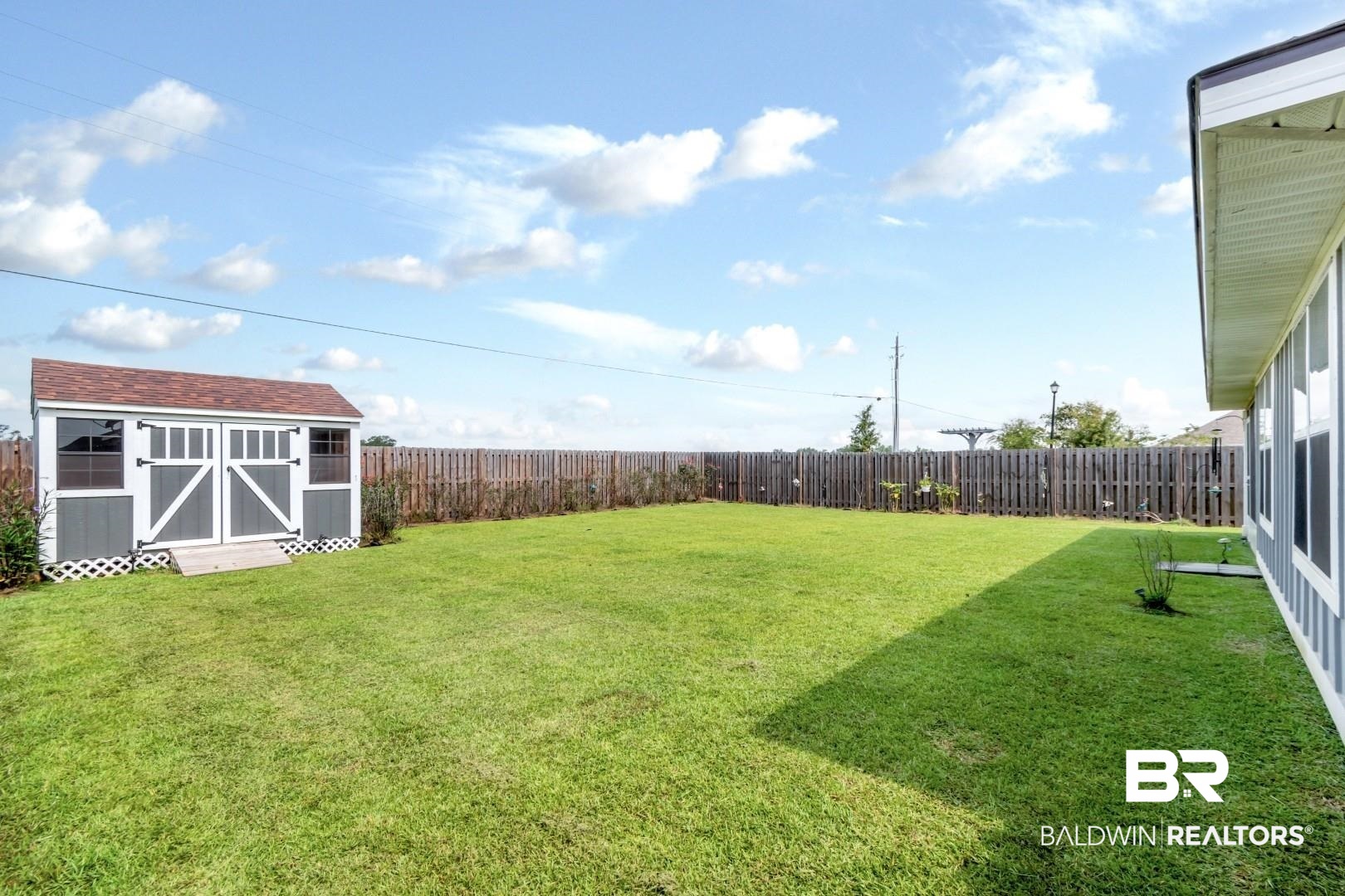 1295 Hayward Loop Foley, AL 36535 - Photo 26 of 29 Expansive fenced backyard featuring a detached storage shed with a shingled roof, double barn doors, and side windows