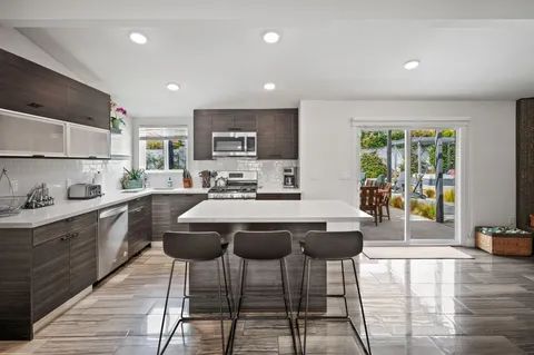 a kitchen with stainless steel appliances granite countertop a stove a sink a refrigerator white cabinets and chairs with wooden floor