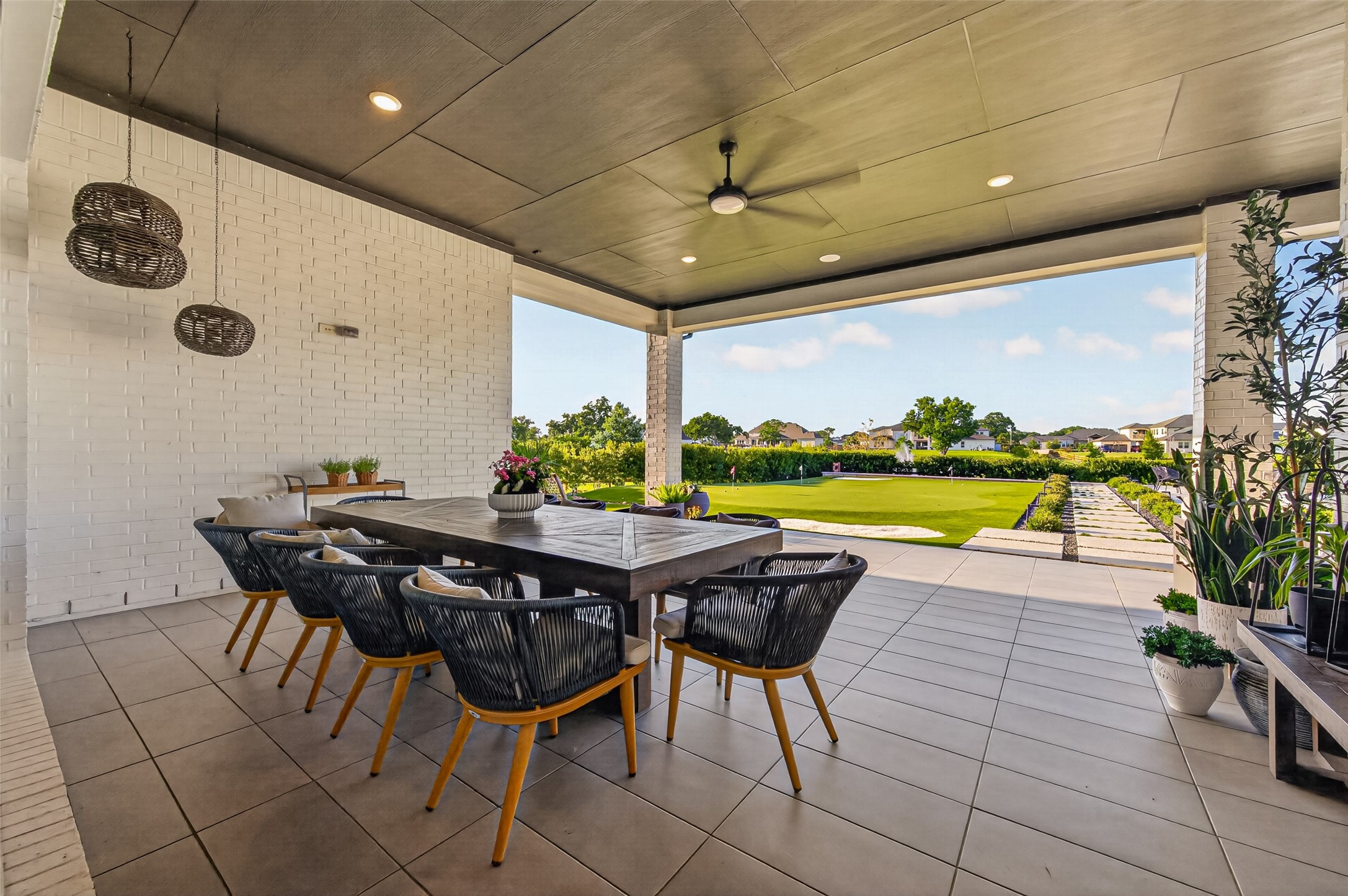 29612 Fulshear Lake Trace Fulshear, TX 77406 - Photo 11 of 48 This spacious covered patio features a stylish dining area with a large table and modern chairs. It offers a serene view of a beautifully landscaped backyard and putting green, perfect for outdoor relaxation and entertainment.