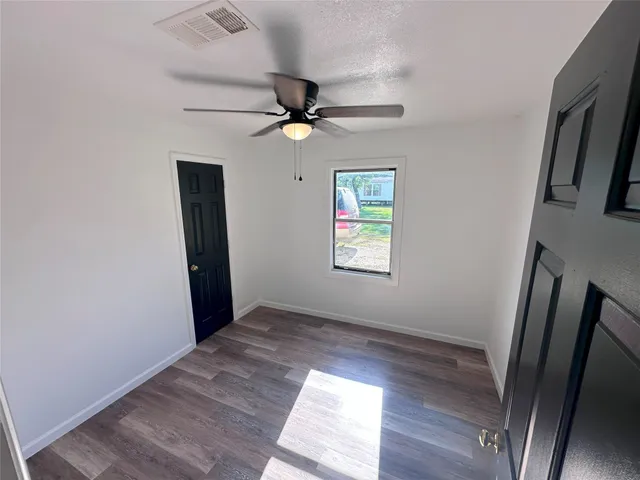 an empty room with wooden floor fan and windows