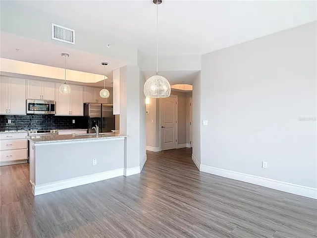 a kitchen with granite countertop a refrigerator oven a sink dishwasher and white cabinets with wooden floor