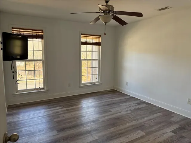 an empty room with wooden floor fan and windows