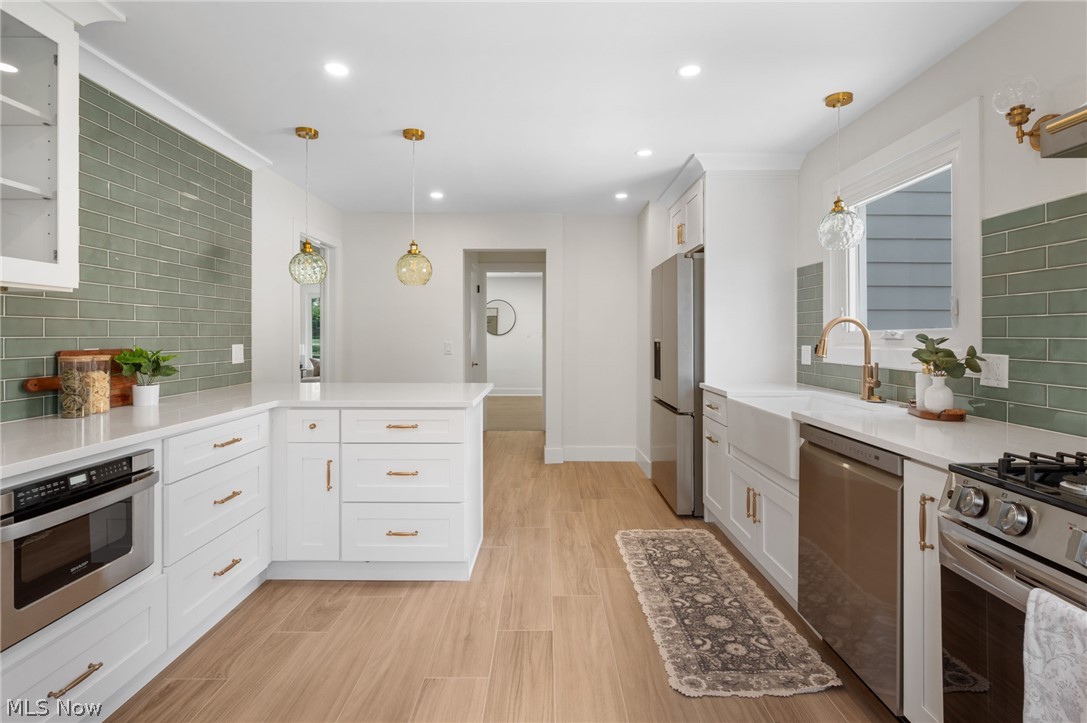 22625 Rye Road Shaker Heights, OH 44122 - Photo 13 of 38 Contemporary kitchen featuring white cabinetry, light-toned wood-finish flooring, a farmhouse sink, stainless steel appliances, and a green subway tile backsplash