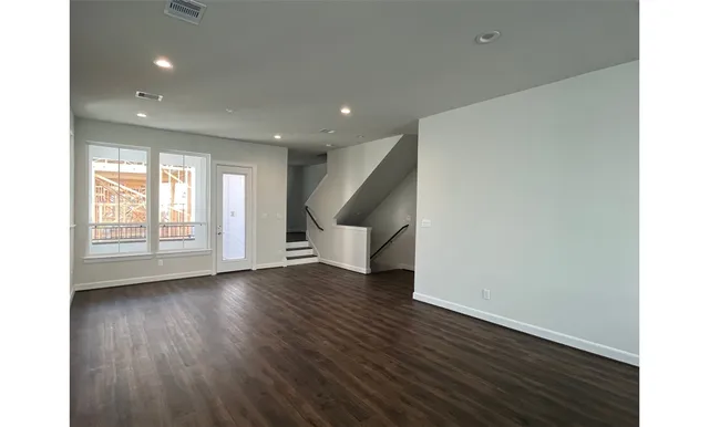 a view of an empty room with wooden floor and stairs