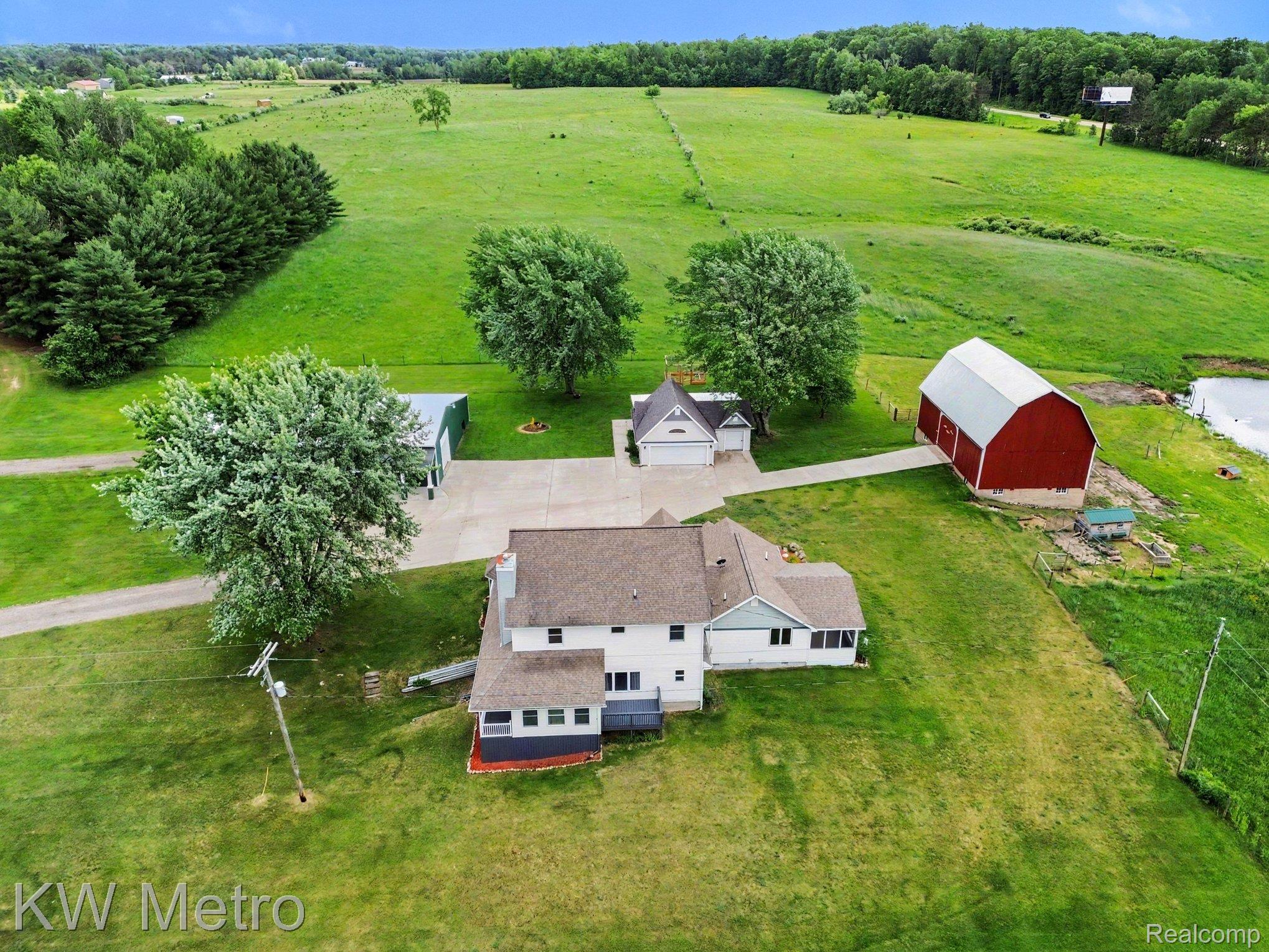 2682 East Haskell Lake Road Harrison, MI 48625 - Photo 7 of 61 Expansive property featuring a white residence with a brown shingle roof, a detached garage, a red barn, and a green metal outbuilding, all set amidst verdant fields and mature trees