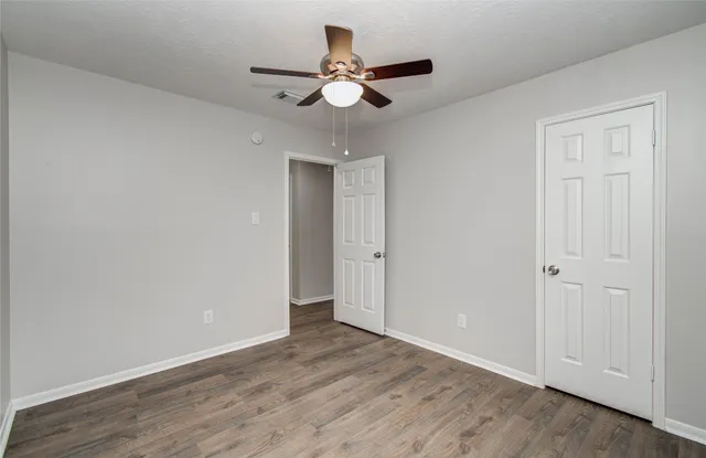an empty room with wooden floor ceiling fan and windows