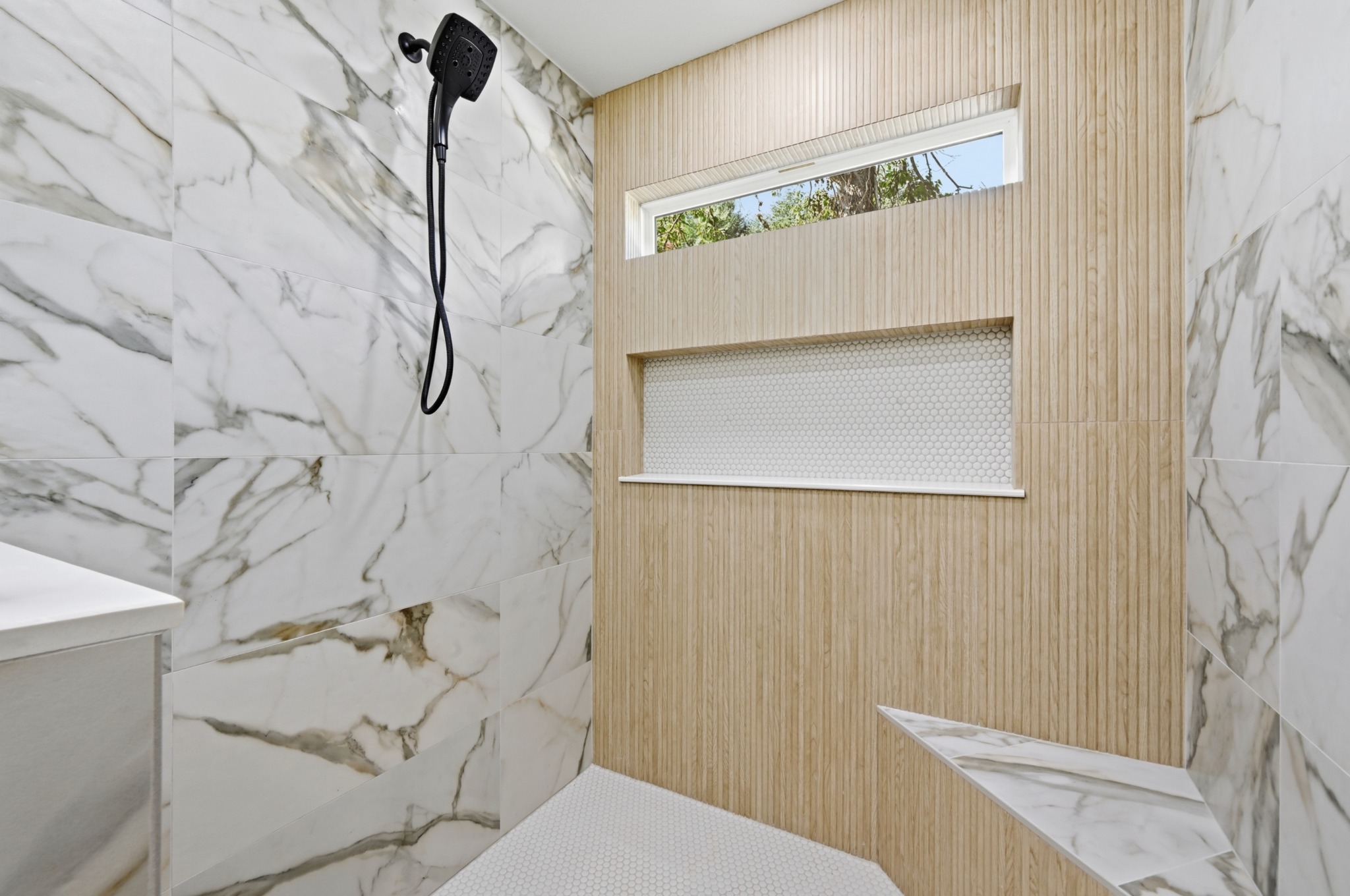 8102 Fort Sumter Road Austin, TX 78745 - Photo 18 of 28 Luxurious walk-in shower features elegant marble and wood-look tile, complete with a built-in bench and recessed shelving.