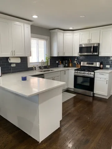 a kitchen with stainless steel appliances granite countertop a stove top oven a sink a refrigerator a white cabinets and wooden floor