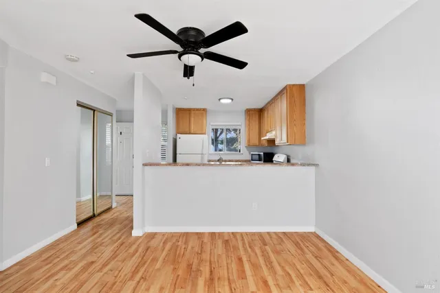 a big room with wooden floor a ceiling fan and kitchen view