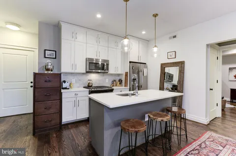 a kitchen with stainless steel appliances granite countertop a stove top oven a sink a dining table and chairs with wooden floor