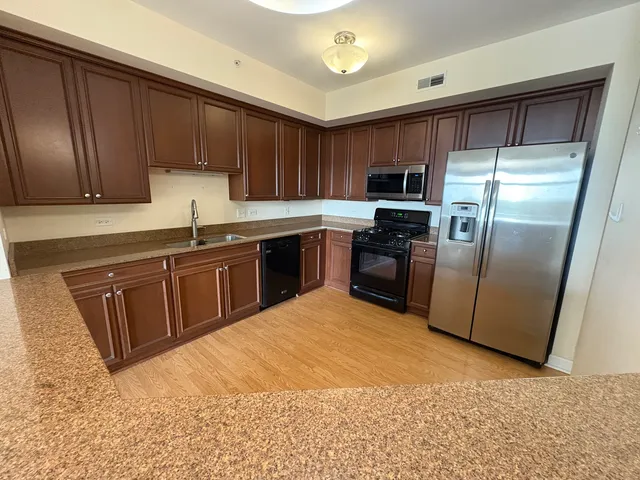 a kitchen with stainless steel appliances granite countertop a refrigerator a sink a stove top oven and cabinets