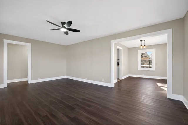 an empty room with wooden floor chandelier fan and windows