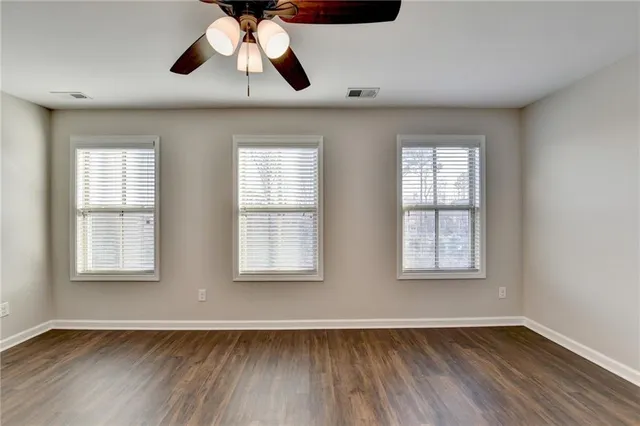 an empty room with wooden floor chandelier fan and windows