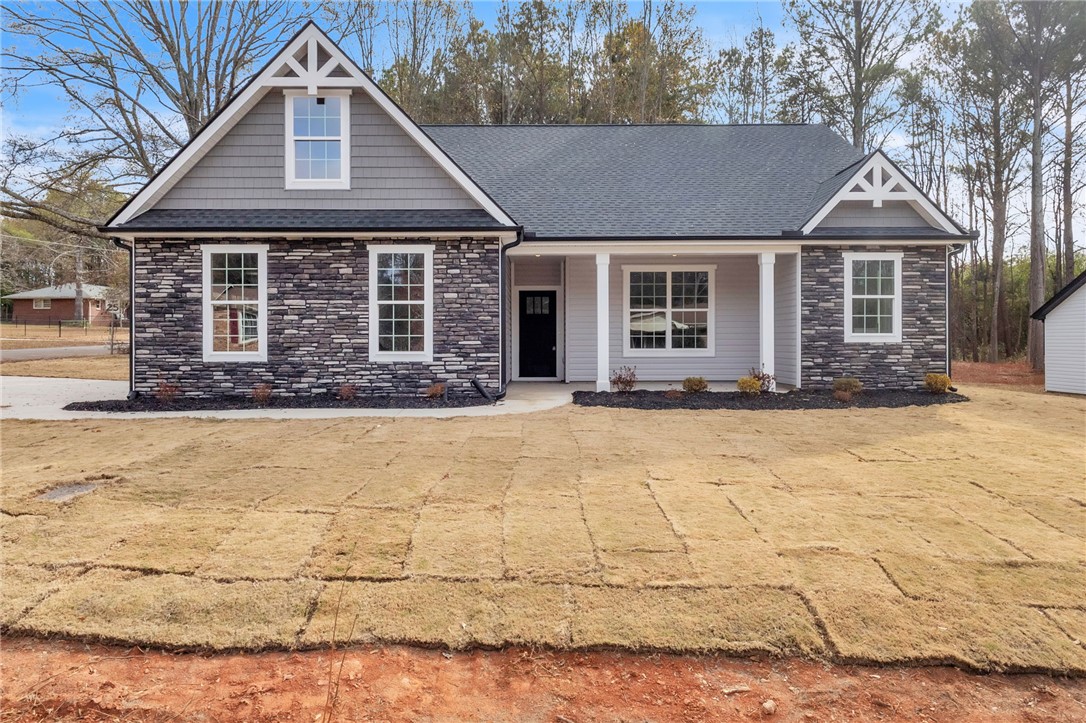 Craftsman inspired home with stone siding, a porch, roof with shingles, and a front lawn