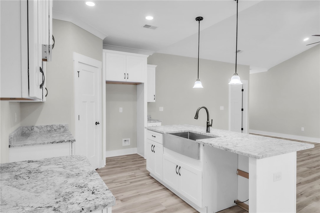 121 Ashley Drive Pelzer, SC 29669 - Photo 9 of 25 Kitchen with light wood-style flooring, light stone countertops, a center island with sink, decorative light fixtures, and white cabinetry