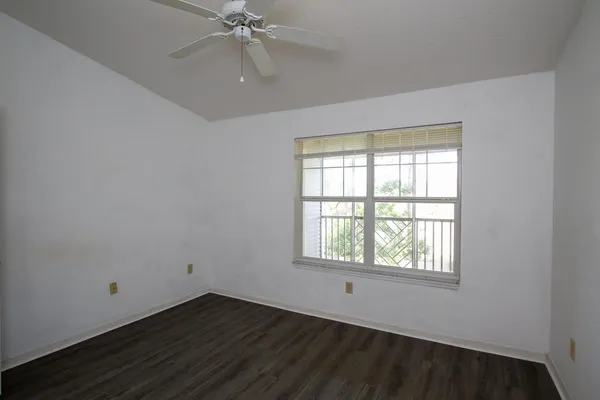 an empty room with wooden floor windows and fan