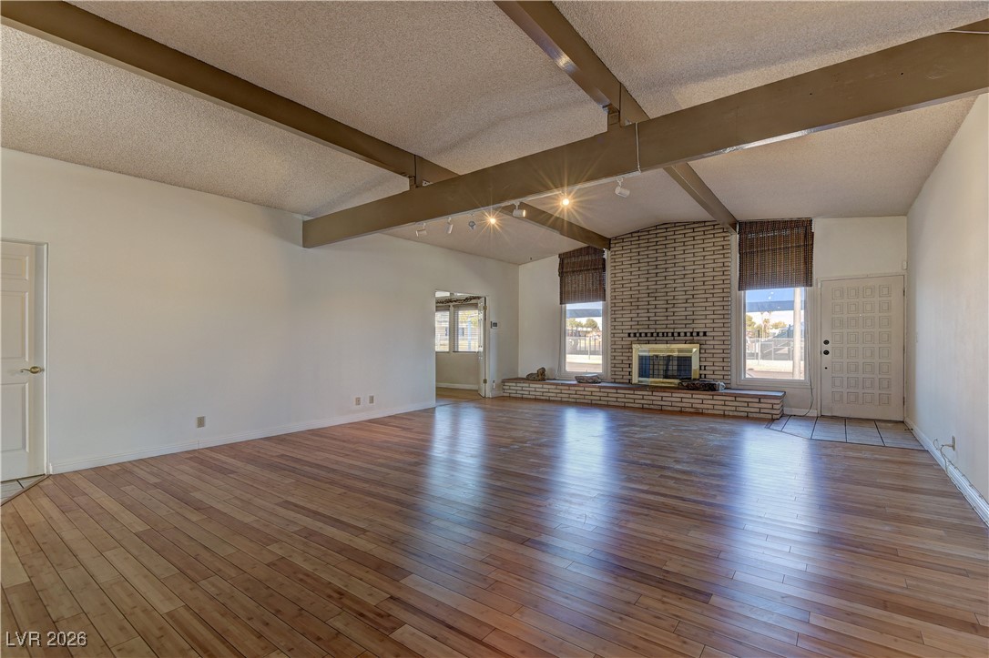 6309 Rassler Avenue Las Vegas, NV 89107 - Photo 4 of 19 Unfurnished living room with light wood-style floors, a fireplace, rail lighting, plenty of natural light, and a textured ceiling