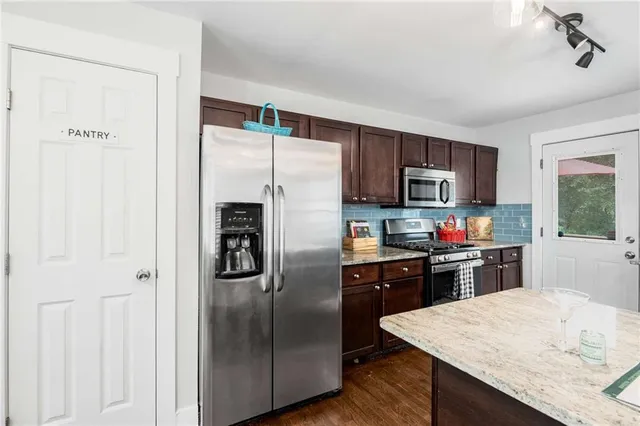 a kitchen with stainless steel appliances granite countertop a sink a stove a refrigerator cabinets and chairs