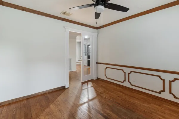 a view of an empty room with wooden floor and a ceiling fan