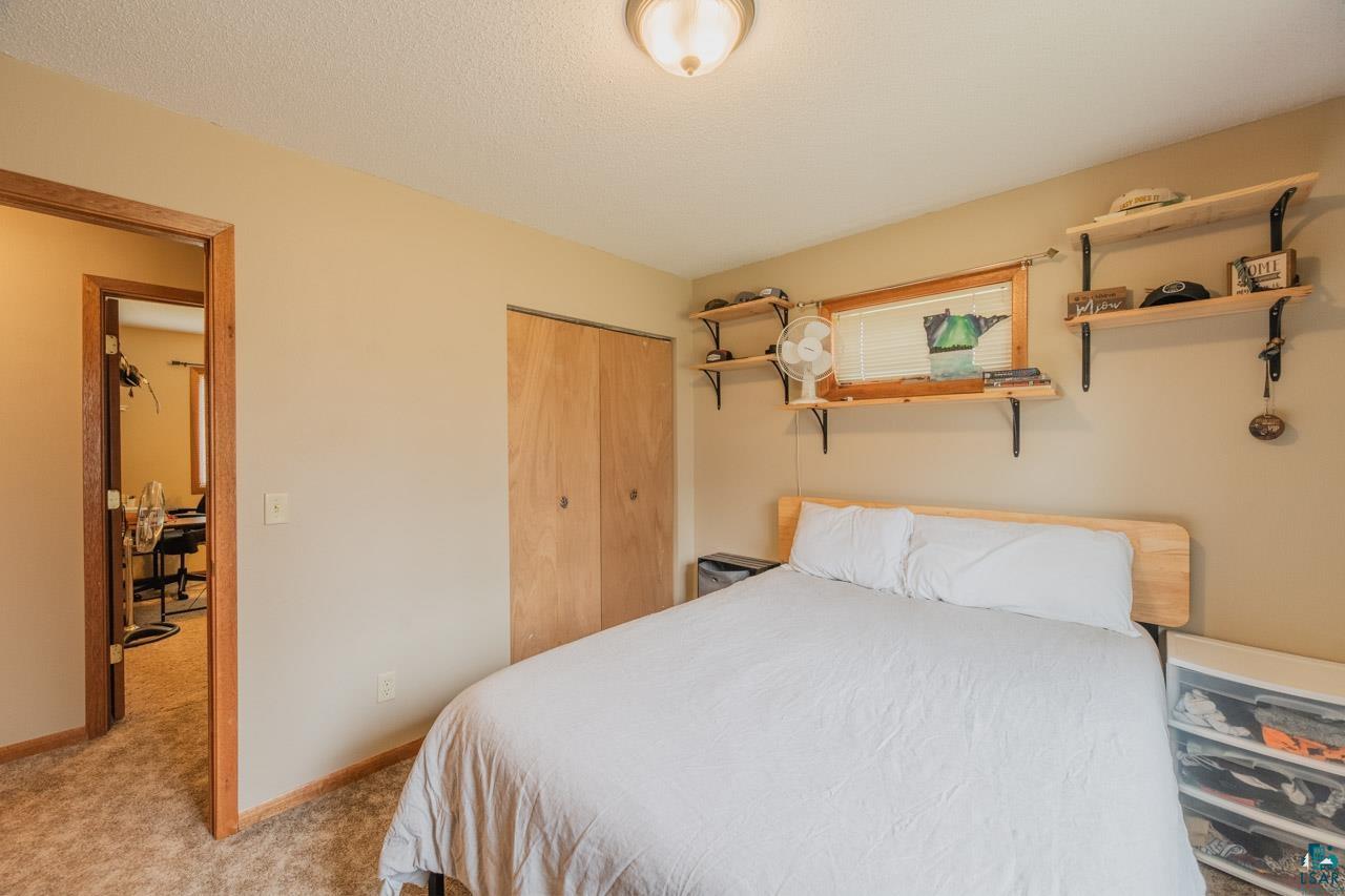 228 3rd Street Southeast Cook, MN 55723 - Photo 12 of 30 Bedroom featuring wood-finish bi-fold closet doors, wall-to-wall carpeting, a wood-trimmed window, and a flush-mount ceiling light