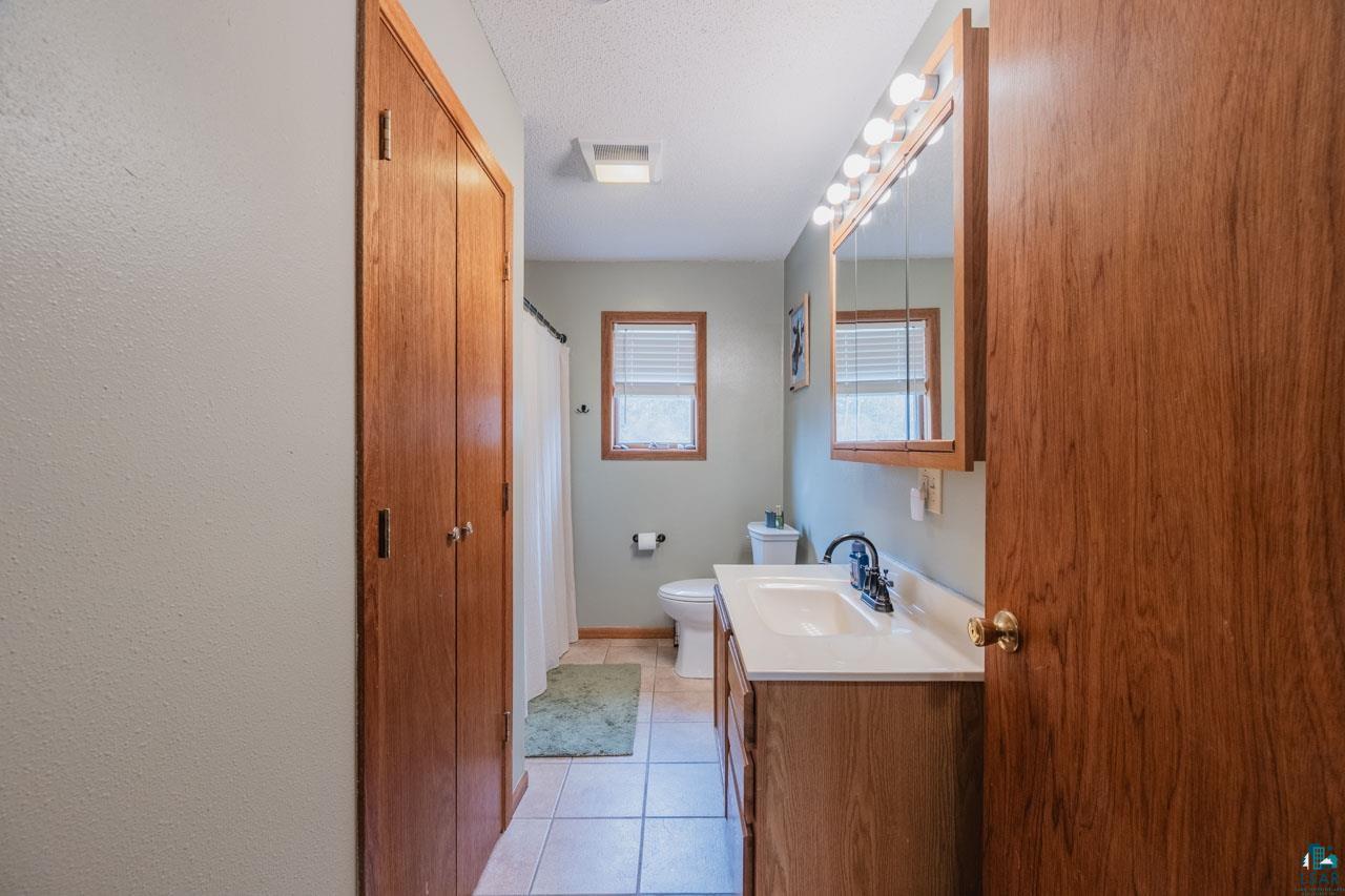 228 3rd Street Southeast Cook, MN 55723 - Photo 14 of 30 Full bathroom featuring a single vanity with an integrated sink, a large mirror with vanity lighting, and a window with blinds