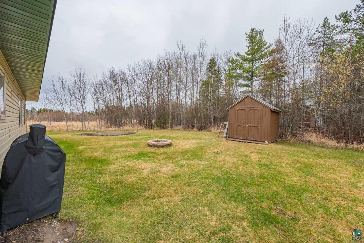228 3rd Street Southeast Cook, MN 55723 - Photo 18 of 30 Expansive grassy yard featuring a brown wood-paneled shed, a circular fire pit, and mature trees surrounding the perimeter