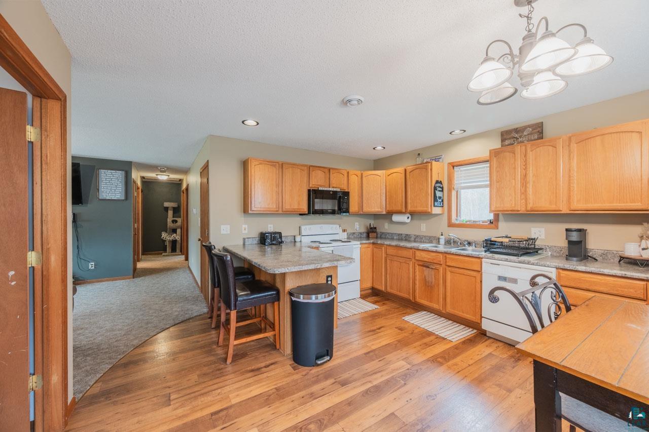 228 3rd Street Southeast Cook, MN 55723 - Photo 2 of 30 Kitchen featuring wood-finish flooring, light wood cabinetry, white appliances, and a granite-style countertop