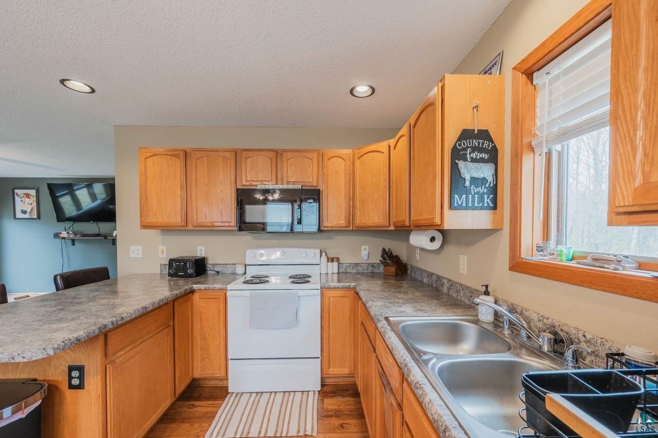 228 3rd Street Southeast Cook, MN 55723 - Photo 3 of 30 Kitchen featuring light wood cabinetry, a double basin stainless steel sink, a built-in microwave, and a white electric range