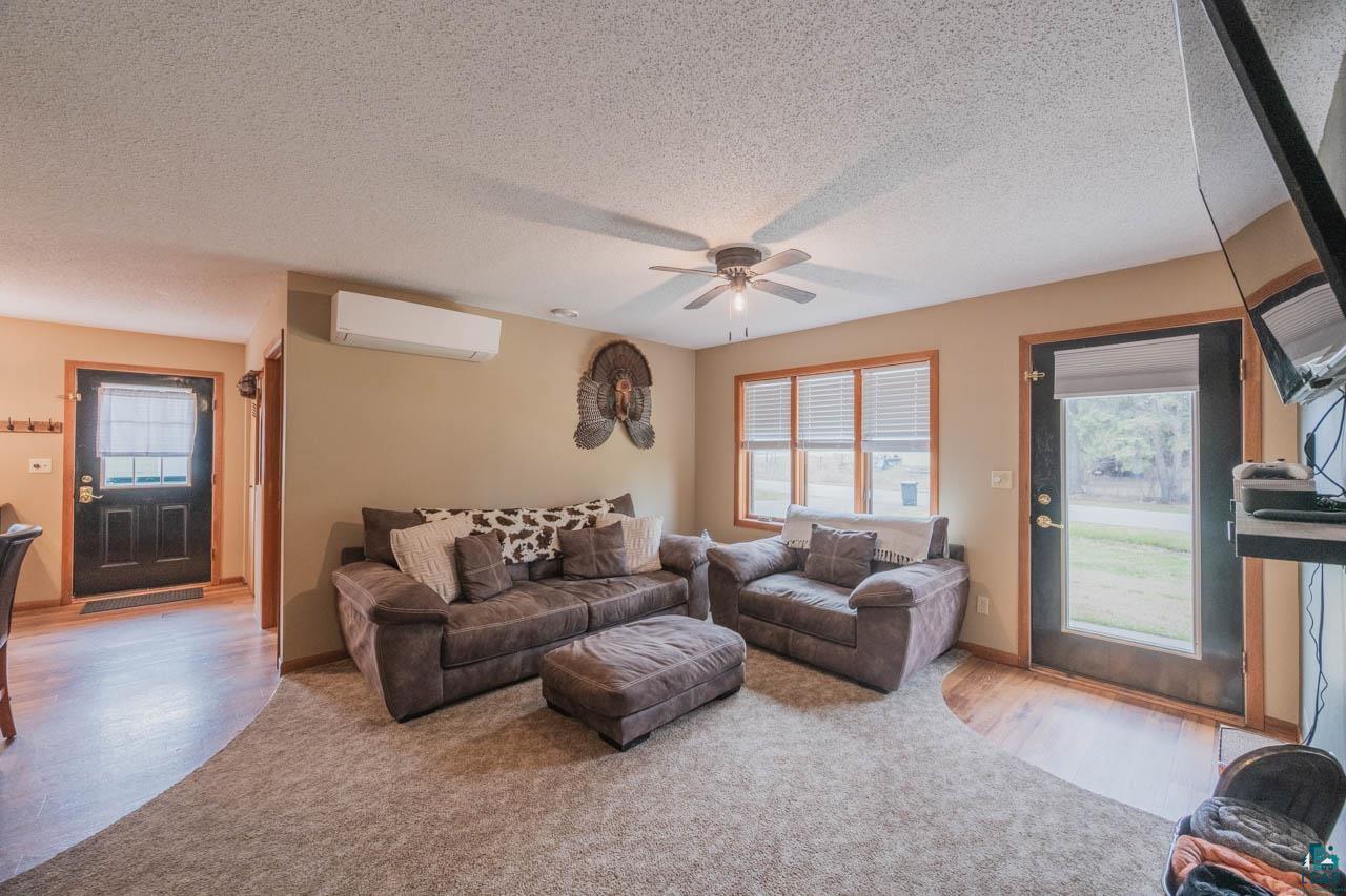 228 3rd Street Southeast Cook, MN 55723 - Photo 7 of 30 Open living area featuring wood-finish flooring, a wall-mounted mini-split system, a ceiling fan with integrated lighting, and multiple windows with blinds