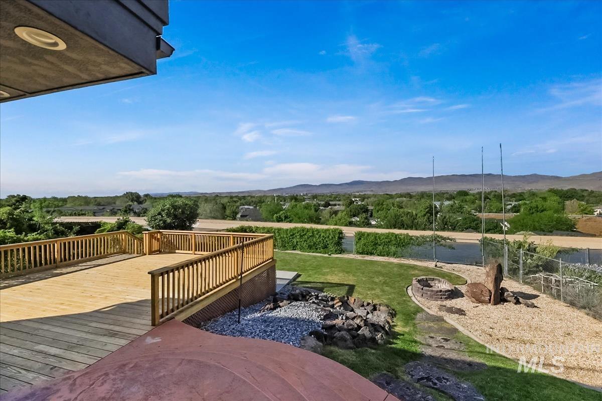 2804 West Sunrise Rim Road Boise, ID 83705 - Photo 49 of 50 Expansive wood deck with natural wood railings, recessed lighting, a gravel fire pit area, and landscaped backyard with mature greenery