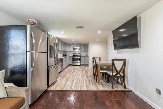 a kitchen with stainless steel appliances granite countertop a refrigerator a microwave oven a sink a dining table and chairs with wooden floor