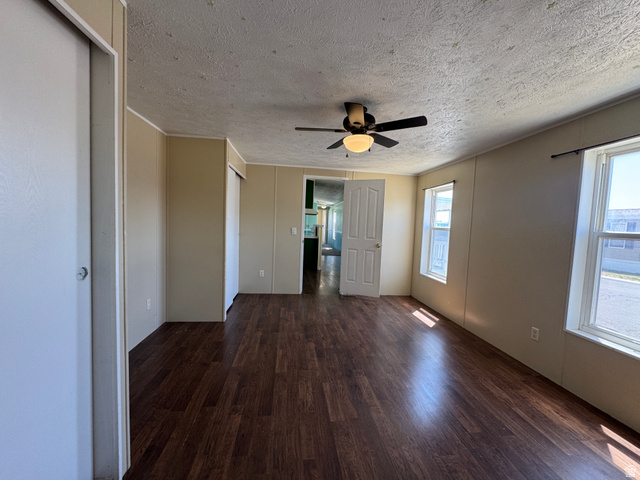 2491 Highway 89, Unit 315 Pleasant View, UT 84404 - Photo 12 of 34 Spacious interior room featuring wood-finish flooring, two windows with white trim, a ceiling fan with light fixture, and two built-in closet doors