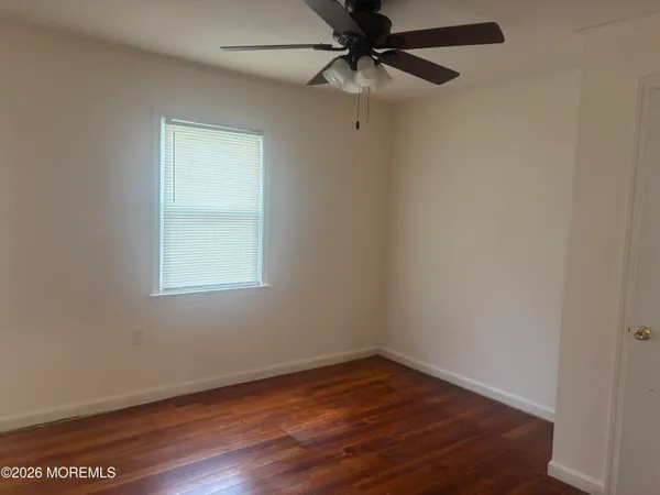 an empty room with wooden floor fan and windows