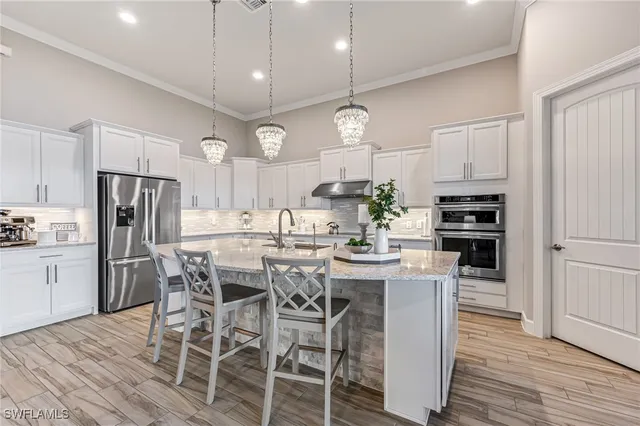 a kitchen with stainless steel appliances kitchen island granite countertop a dining table chairs refrigerator and sink