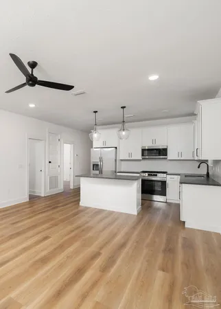 a large kitchen with kitchen island a stove a sink dishwasher a refrigerator and white cabinets with wooden floor