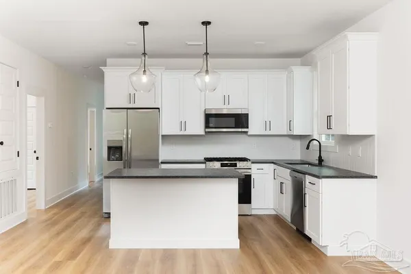 a kitchen with stainless steel appliances granite countertop a sink a stove a refrigerator and island with wooden floor