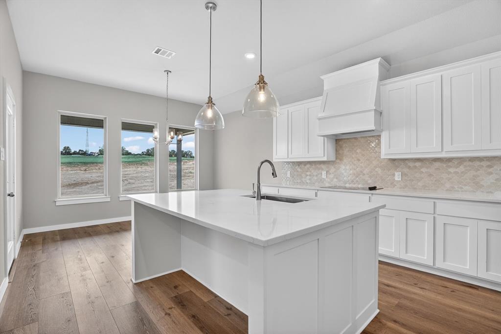 504 Clifton Court Springtown, TX 76082 - Photo 11 of 36 Kitchen featuring a central island with an undermount sink and gooseneck faucet, white shaker-style cabinetry, a decorative range hood, and a textured tile backsplash