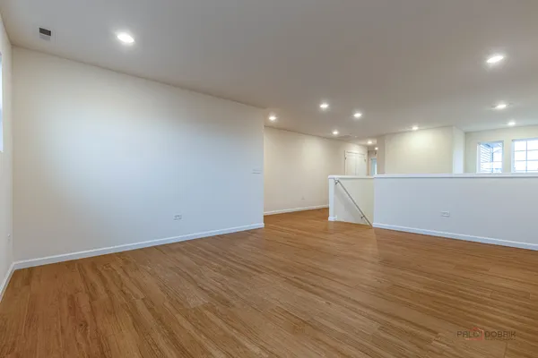 a view of an empty room with wooden floor and kitchen