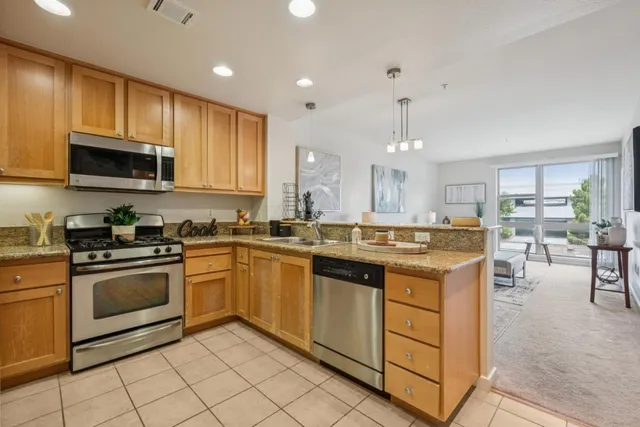 a kitchen with stainless steel appliances granite countertop a stove top oven a sink dishwasher a dining table and chairs with wooden floor