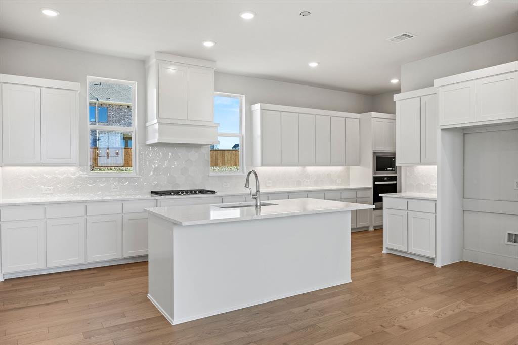 505 Callum Parkway Celina, TX 75009 - Photo 8 of 34 a kitchen with kitchen island a sink a stove a refrigerator and white cabinets