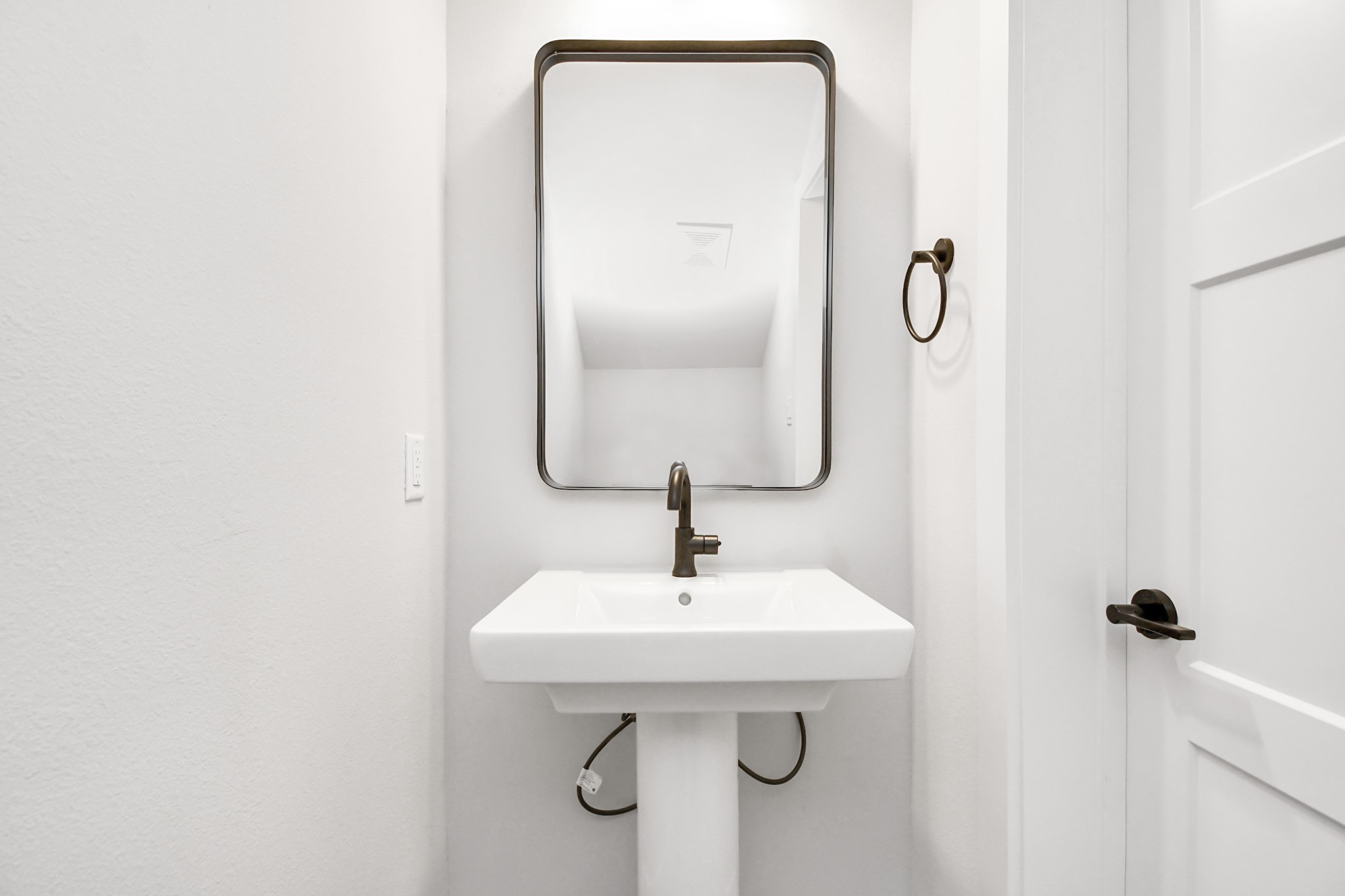 313 Charlock Street Houston, TX 77022 - Photo 14 of 34 This photo shows a compact, modern half-bathroom featuring a sleek pedestal sink, a rectangular mirror, and white walls, offering a clean and minimalist design.