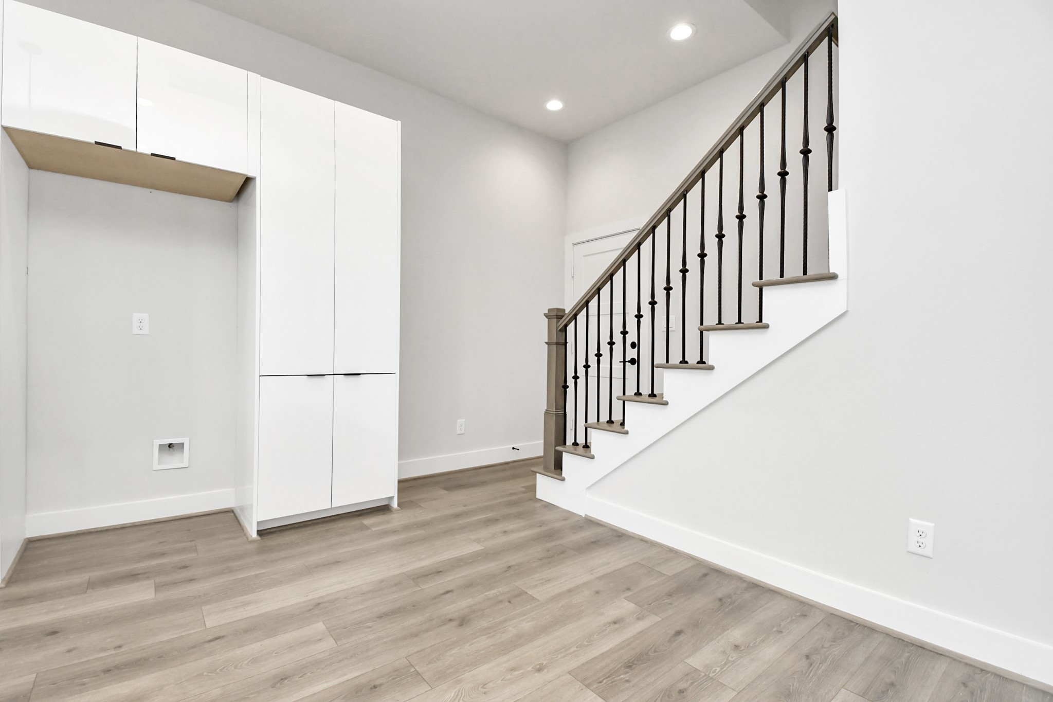 313 Charlock Street Houston, TX 77022 - Photo 15 of 34 This modern space features sleek white cabinetry and a stylish staircase with dark railings, complemented by light wood flooring and neutral walls, creating a bright and contemporary atmosphere.