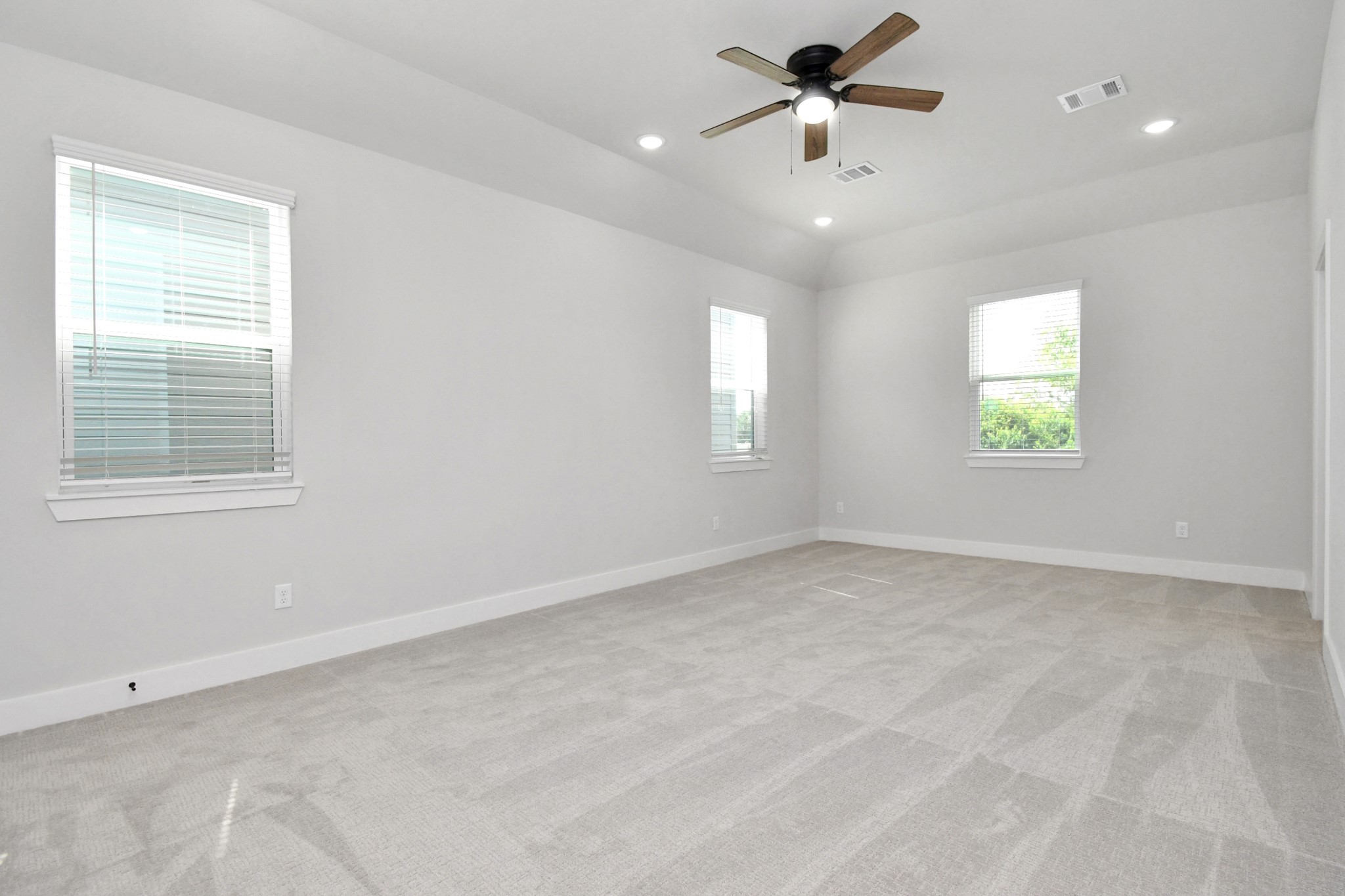 313 Charlock Street Houston, TX 77022 - Photo 17 of 34 Spacious, bright room with light gray walls and carpet, featuring three windows with blinds. A ceiling fan and recessed lighting add functionality and style.