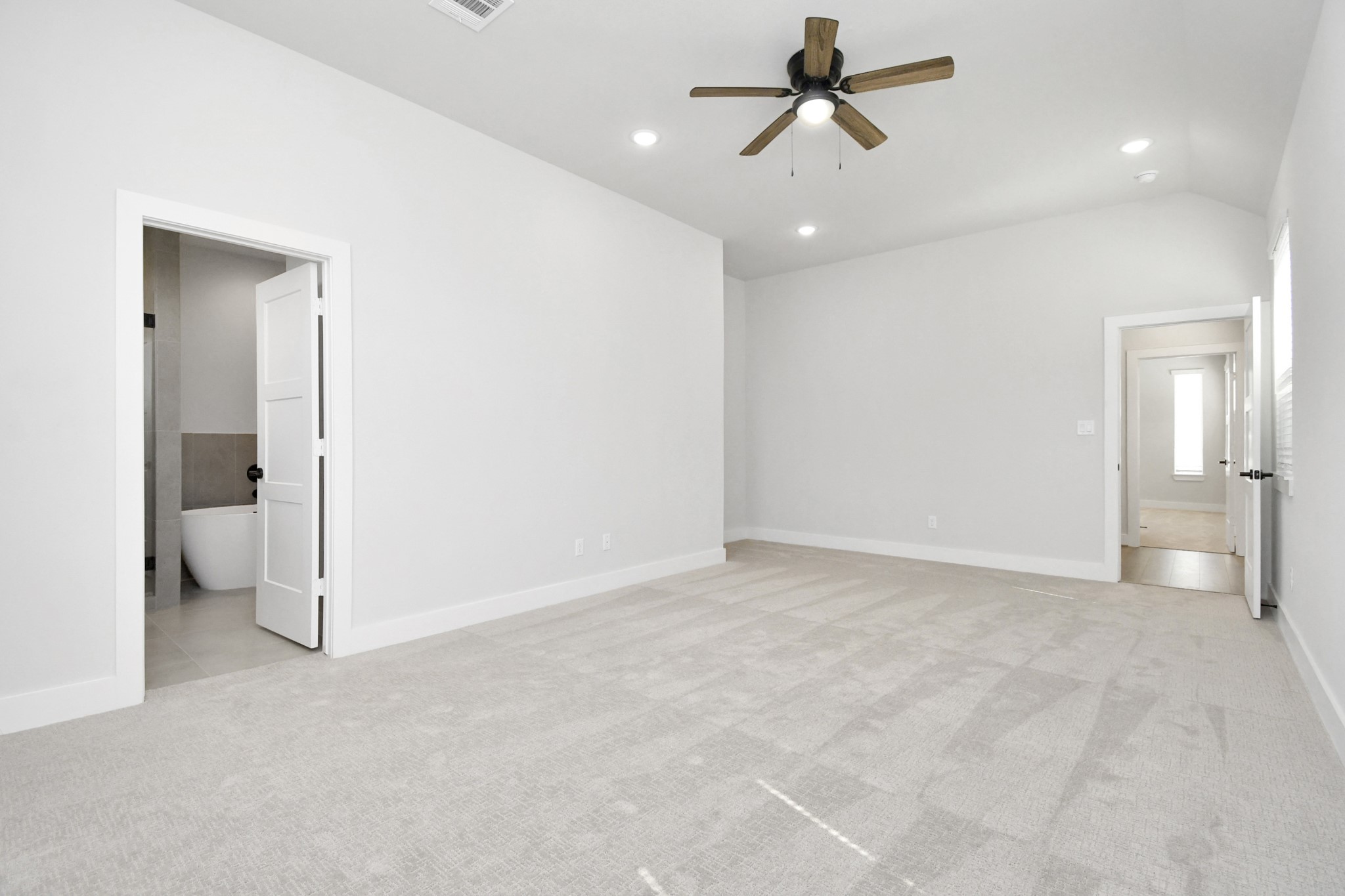 313 Charlock Street Houston, TX 77022 - Photo 18 of 34 This spacious bedroom features soft carpet flooring, a ceiling fan, and recessed lighting. It includes an en-suite bathroom with a modern freestanding tub and a connecting hallway.