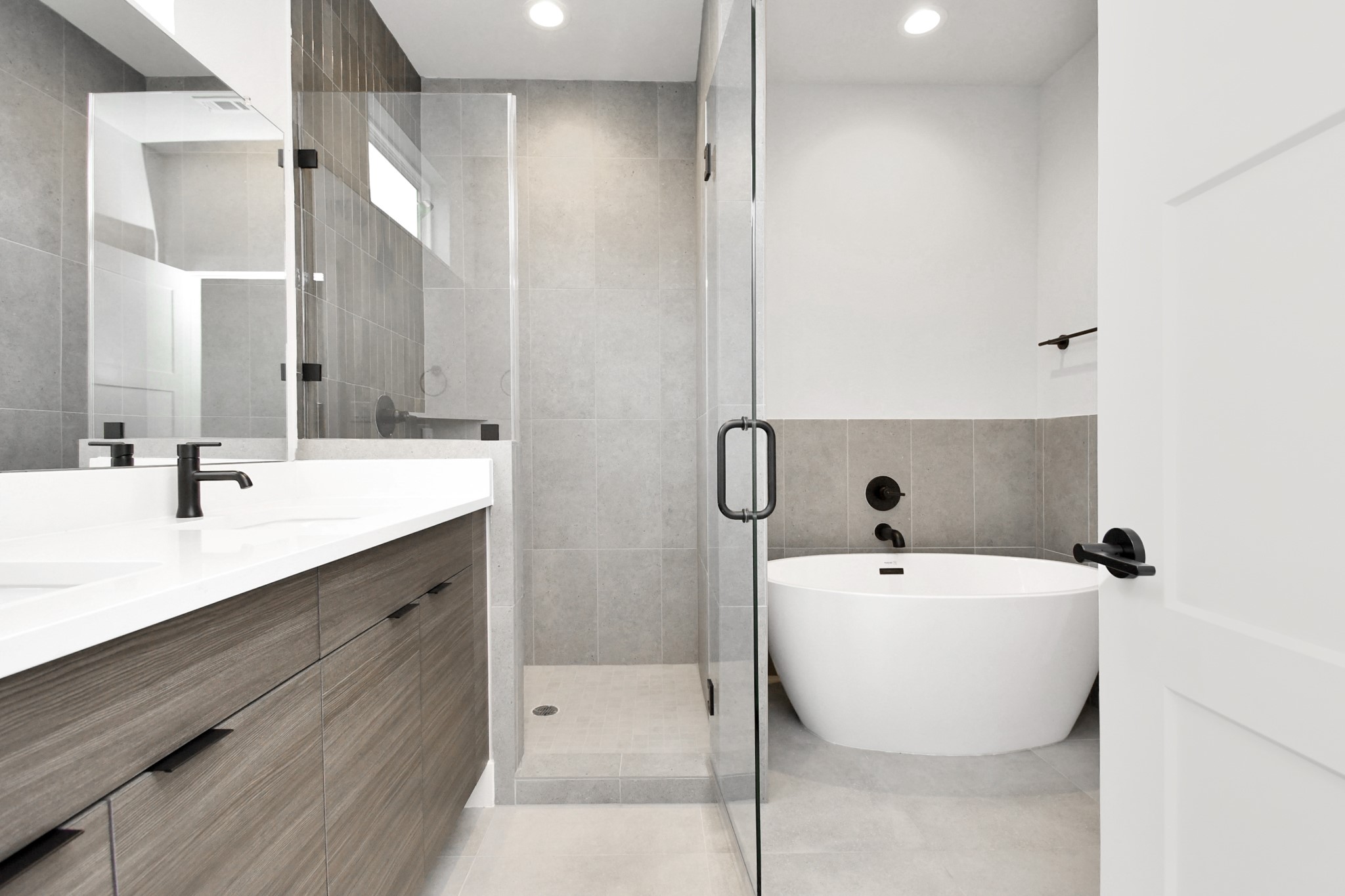 313 Charlock Street Houston, TX 77022 - Photo 19 of 34 This bathroom features a modern design with a sleek glass shower, a freestanding bathtub, and a double vanity with black fixtures. The neutral tile and wood cabinetry create a clean, contemporary look.